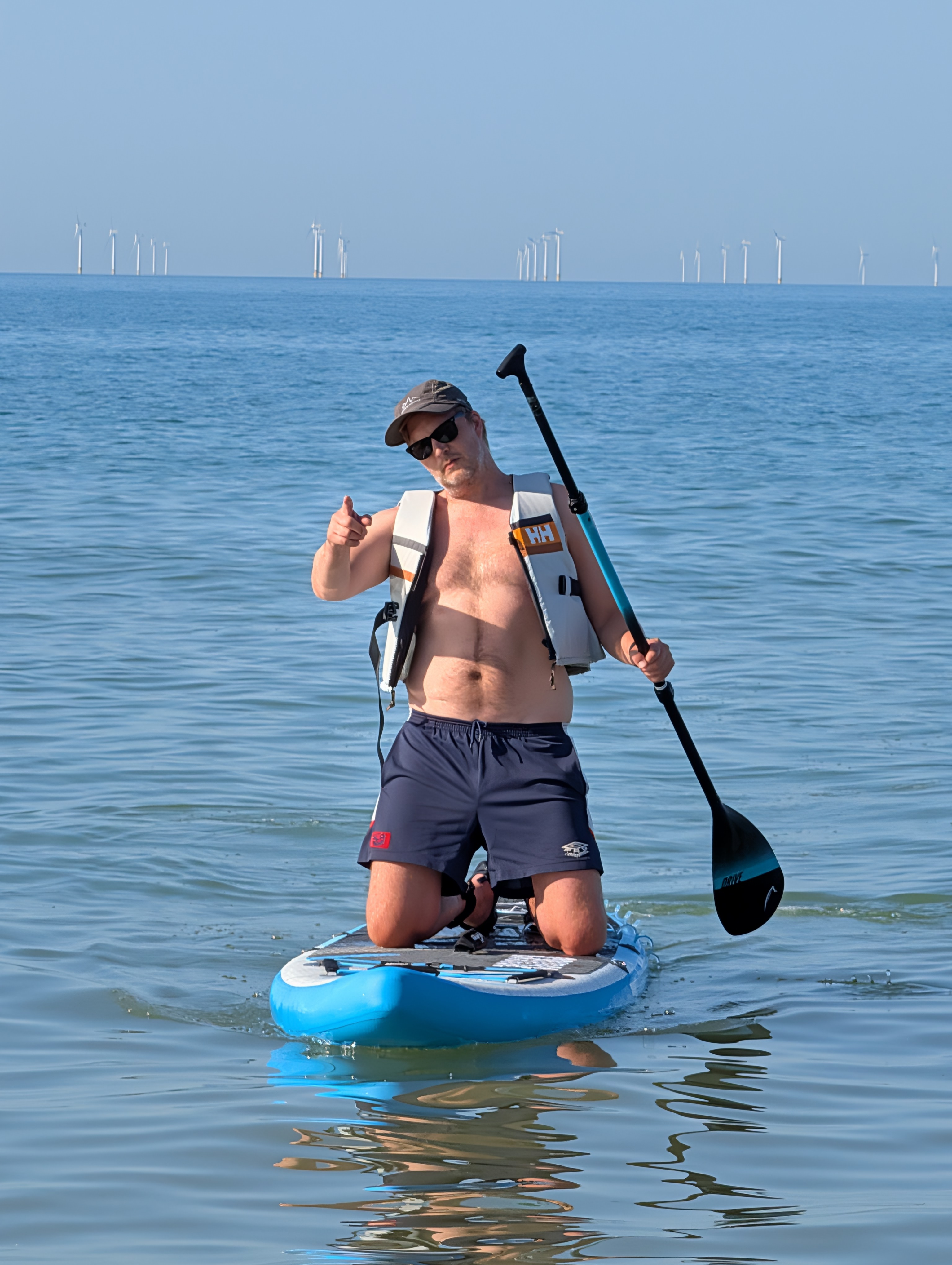 Paddleboarder giving thumbs up with windfarm in background